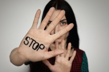 Young woman with word STOP written on her palm against light bac